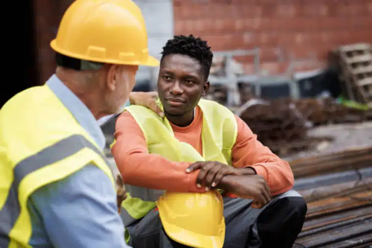 senior man consoling his colleague at construction site - sad blue collar worker. Manager taking accountability.