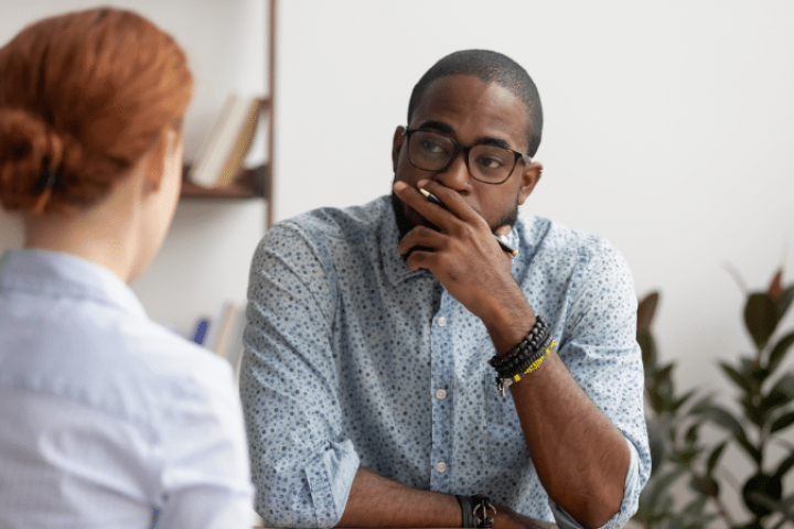 Man sitting to listen to coworker communicating work concerns.