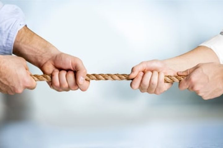 Business people pulling rope in opposite directions at office