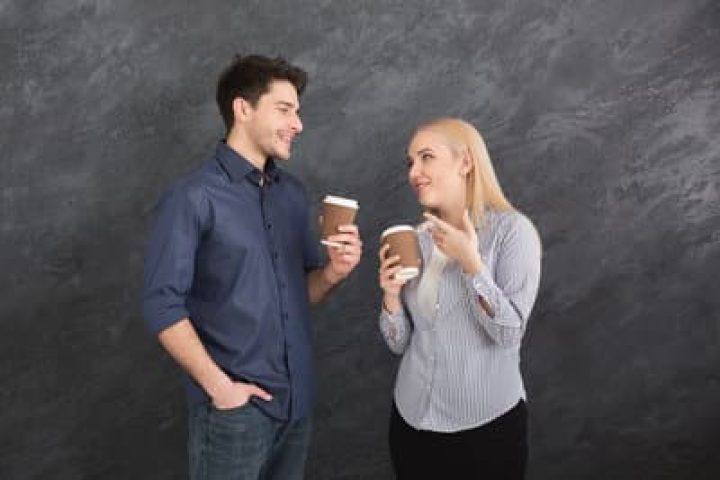 Coffee break. Couple of young colleagues drinking coffee, having nice talk, gray studio background, copy space
