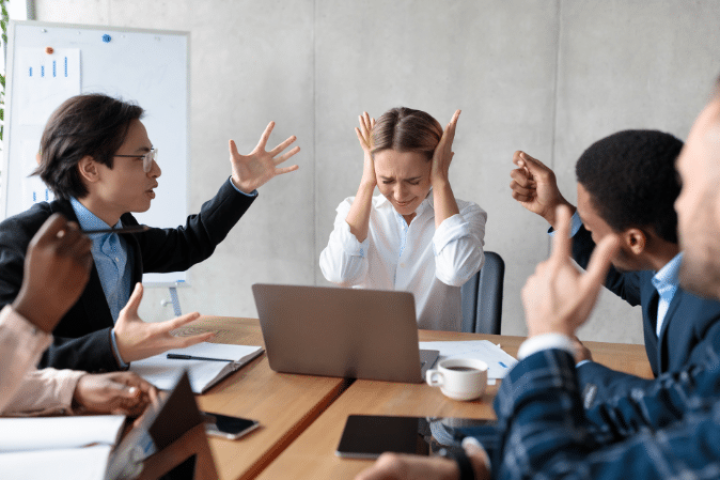 Workplace conflicts arise in meeting as a group flails hands and one covers ears.